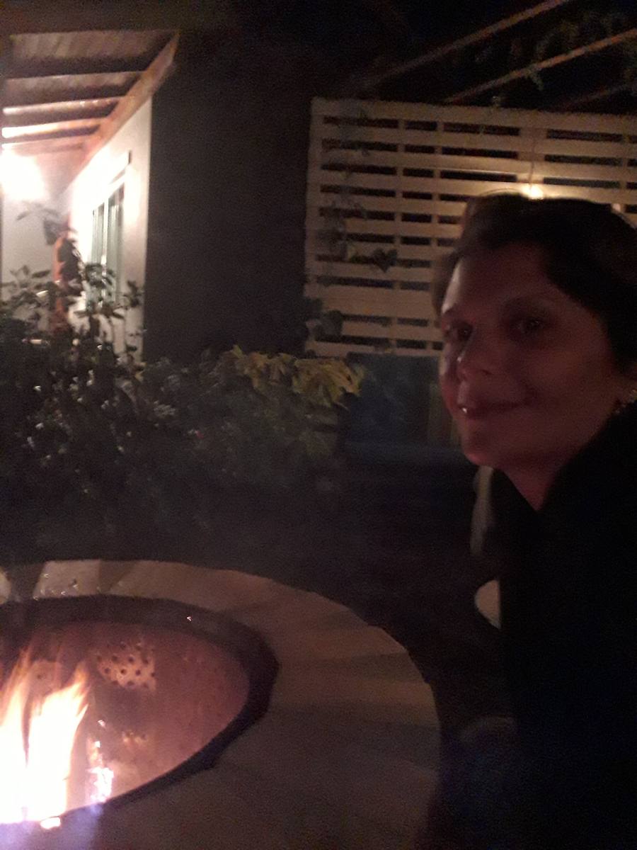 Milla Camata sentada ao lado de uma fogueira acesa em um jardim, à noite