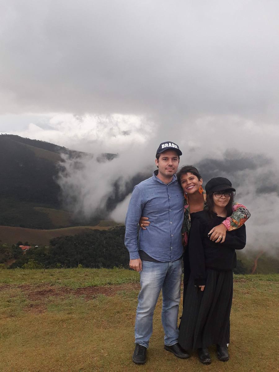 Milla Camata com a família em um mirante, com nuvens densas transbordando sobre a serra ao fundo