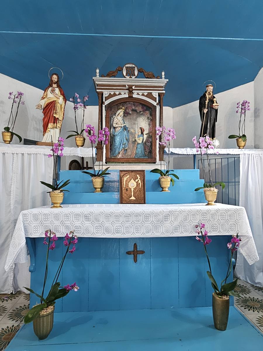 Interior da Igrejinha do Caravaggio, com altar em azul e branco, orquídeas e a imagem da santa no nicho central