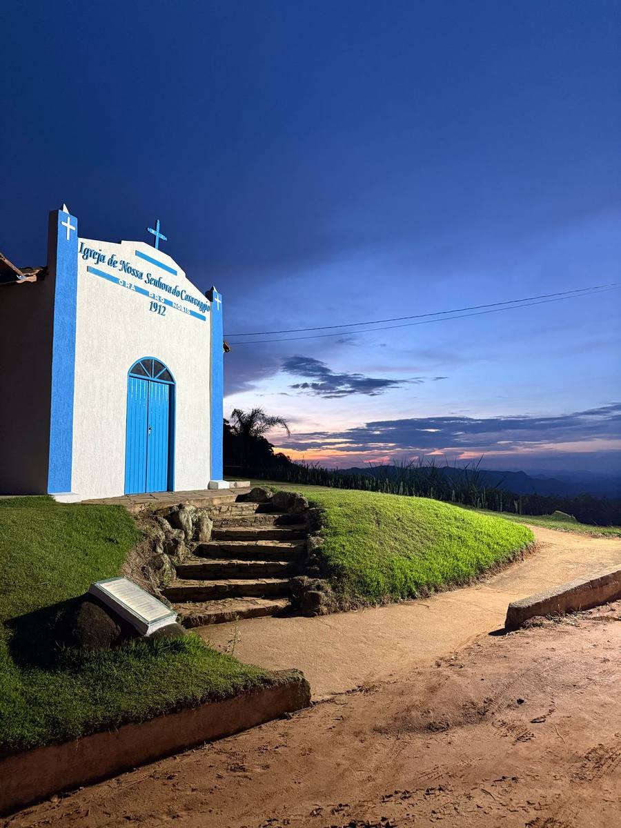 Igrejinha do Caravaggio, capela branca com detalhes azuis e a inscrição de 1912, fotografada ao anoitecer no alto do vale