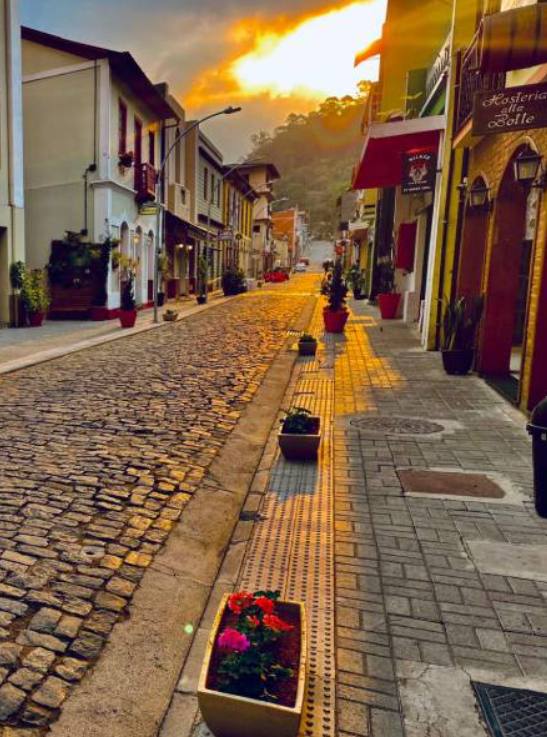 Calçamento em pedra e casarões coloridos da Rua do Lazer ao entardecer, com vasos de flores ao longo da calçada