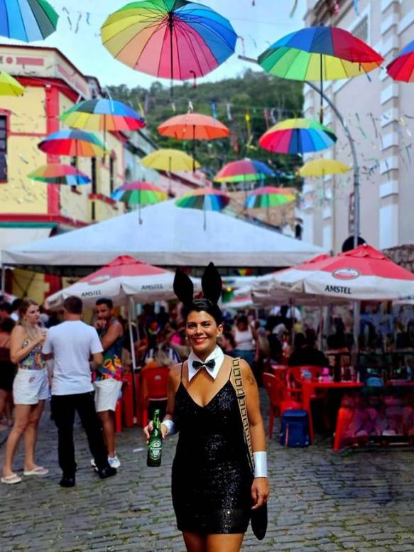 Guarda-chuvas coloridos suspensos sobre o calçamento da Rua do Lazer durante uma festa, com mesas ocupadas ao fundo
