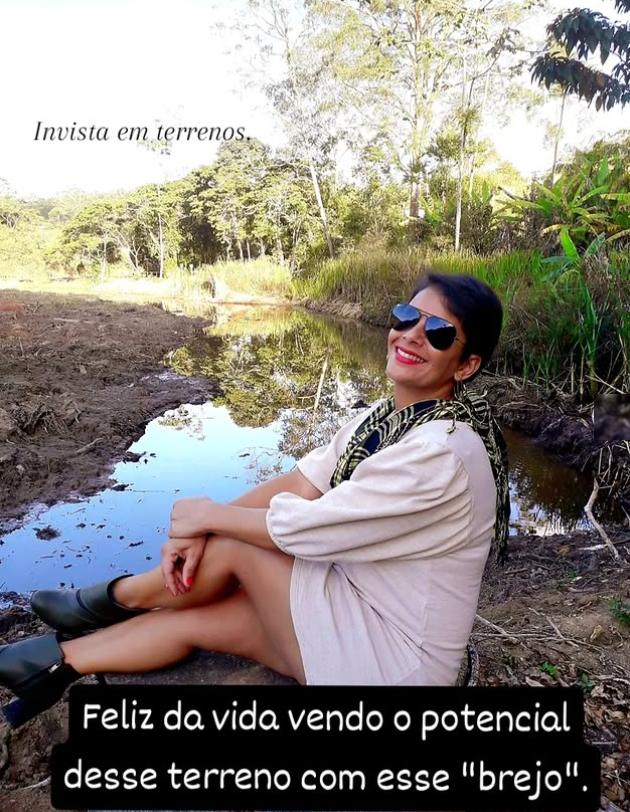 Milla sentada de frente para uma área de terra batida com um curso d'água raso ao fundo, antes das melhorias no terreno