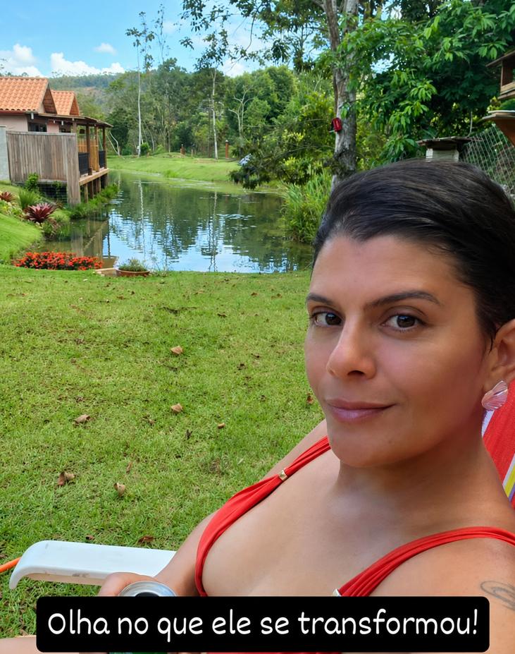 Milla tomando sol com um lago, grama verde, canteiro de flores vermelhas e a casa ao fundo, no mesmo terreno depois das melhorias